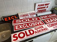Photo showing multiple real estate signs with red and white text, including SOLD, EXCLUSIVE, COMING SOON, FOR LEASE, LEASED, SOLD OVER ASKING, PLEASE WAIT SHOWING IN PROGRESS, and OPEN HOUSE.