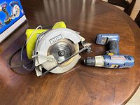 Photo showing Ryobi circular saw with attached power cord next to blue Ryobi cordless drill without battery