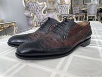 Pair of men's dress shoes handmade in Italy by Salvatore Ferragamo, black leather and brown alligator skin with wingtip brogue design and perforated details.