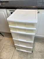Full view of white plastic storage unit with four drawers on wheels, showing size and condition.