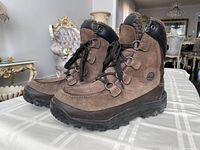 Pair of brown Timberland winter boots angled left, showing side profiles, torn pull tab visible on right boot