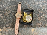 Pink women's wrist watch and gold Swiss pocket watch in a box on countertop