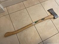 Full view of the axe lying flat on a tiled floor showing the wooden handle and metal head from above.