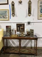Wide shot of table with brass decorative pieces including curio cases, wall sconces above, mirrored trays, vase, and urn on the table.
