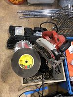 Photo showing Skil electric circular saw with mounted blade, abrasive cutting wheel, and part of car jack in crate.
