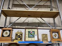 Five tabletop clocks displayed on a shelf including wooden and brass designs, one with Roman numerals and another with a colorful square dial