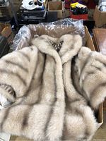 Full view of the light beige faux fur stole laid on a plastic-lined cardboard box, showing the stole's texture and color.