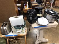 Photo showing four different toasters, a Black & Decker coffee pot, a GoWISE air fryer, a white electric grill labeled 'Lean Mean Fat Grilling Machine', and a large crock pot.