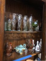 Shelf showing Norman Rockwell collectible bells, ceramic rooster figurines, and a turquoise ceramic teapot with gold floral designs.