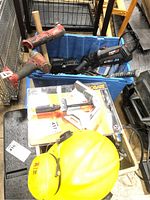 Blue bin with Milwaukee cordless tools (without batteries) and Roto Zip saw with an orange-handled Roto Zip tool front and center, along with a yellow safety helmet and Hobart welding clamp in packaging on a black surface below.