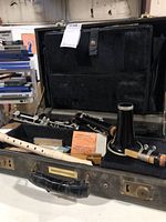 Open black hard case with Selmer clarinet in multiple disassembled pieces and white plastic Yamaha recorder inside, along with some paper labels.