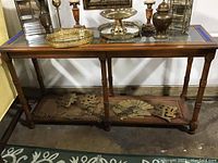 Front view of the glass top sofa table showing the wooden frame, caned lower shelf with gold designs, and turned legs.