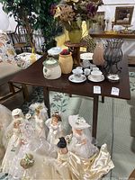 Wooden table shown in a store setting with various other items around. Table surface holds miscellaneous items not included in lot.