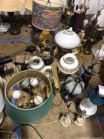 Photo showing multiple assorted table lamps with various bases and shades on floor, including colorful yellow glass lamp and green ribbed shade