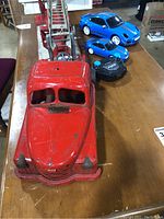 Large vintage red metal Structo fire engine with ladder and three blue Adventure Force remote control cars with black controller on wooden table.