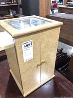 Exterior view of the beige wooden storage chest with glass top, closed doors, and gold knobs for watch storage.