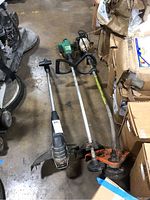 Three weed whips shown together on floor near cardboard boxes. Includes Stihl FS-56, Black & Decker, and Feather Lite models.