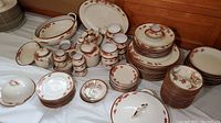 Wide view of the full lot showing stacks of plates, covered bowls, small condiment jars, and other pieces of Asian china with red floral and gold trim design
