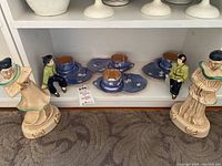 Display of four Asian figurines and three blue Japanese lusterware teacup and saucer sets on white shelf