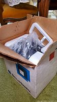Box partially open showing projector inside styrofoam packaging and plastic wrap.