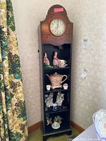 Front view of clock display shelf with built-in clock on top and four display shelves filled with decorative ceramic items.