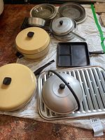 Overview of various cookware items including yellow lidded pots, pie plates, bread pans, cast-iron skillet, stock pot, kettle on a white surface.