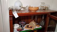 Sideboard with crystal decanter, wood salad bowl, and other glass and serving pieces arranged on top and inside the cabinet