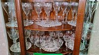 Glass cabinet displaying etched crystal stemware on lace doilies, including wine glasses and champagne coupes.