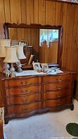 Full view of the wooden dresser with attached mirror showing scratches and stains on the dresser top, photographed in a wood-paneled room.