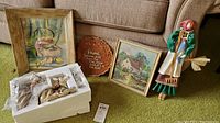 Lot overview showing all items: two framed paintings, wood plaque, figural wall hanging, boxed Fitz & Floyd deer figurines