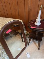 Photo of the wood framed beveled mirror leaning against a bed, showing dark brown frame and beveling with measurement tag visible