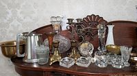 Photo showing a brass bowl, silver-plated tankard, clear cut crystal decanter, brass candle holders, religious figurines, and salt dips.
