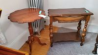 Two vintage wooden side tables together: a tri-foot pedestal table and a rectangular side table with turned legs and lower shelf, medium wood finish, visible wear.