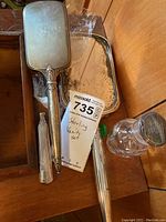 Sterling silver hand mirror, hairbrush, small item, and glass perfume bottle with stopper visible in a wooden drawer.
