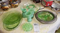 Vaseline glass plates, three jadeite glass egg coddlers, separated round Vaseline glass dish with metal rim and handle on lace tablecloth
