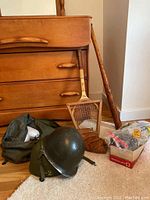Grouping showing one military helmet, army green bag, worn brown leather baseball glove, wooden baseball bat, tennis racket, and golf cleats.