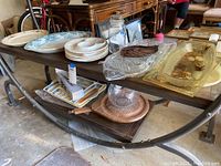 Wide view of multiple platters including ceramic, lucite, wood and glass on a dark metal table.