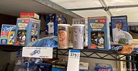 Shelf with multiple boxed Dodger player bobbleheads, cups with player images, and Dodgers snow globe.