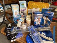 Full view of multiple Dodgers memorabilia items arranged on a table including bobbleheads, cups, hats, watches, and baseball souvenirs.