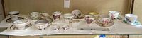 Wide view of all 12 English china teacups with matching saucers in various floral and decorative patterns placed on a white cloth surface.