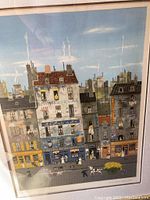 Framed colorful French cityscape print artwork signed B showing street buildings and figures under glass with reflection.
