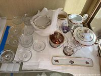 Wide view of lot showing clear ribbed glass dishes, silver covered bowl, purple decorative bowl, clear glass creamer, and white porcelain Limoges pieces with floral patterns.