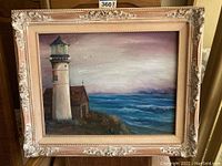 Full front image showing the oil painting of a lighthouse by the ocean in a decorative frame.