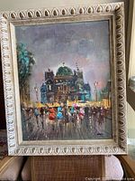 Front view of original signed oil painting featuring a nighttime cityscape with people in colorful attire and an ornate cream-colored frame.