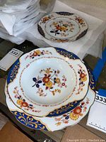 Multiple plates stacked showing floral decoration and blue-gold border design with a close-up view.