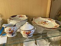 Display of dinnerware set on shelf including serving bowls, 14 inch platters, sugar dish, and creamer with floral and cobalt blue decorative pattern
