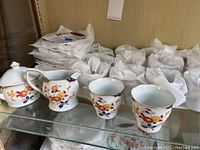 View of sugar dish with lid, creamer, and two teacups showing floral design and gold trim