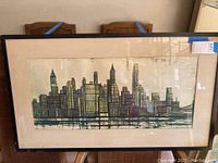 Full view of framed cityscape artwork showing skyline illustration, black frame and beige mat.