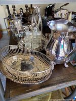 Overview of silver plated serving pieces including water pitcher, bread basket, condiment set with glass bottles, and salad set
