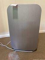 Front view of the silver Allen BreatheSmart Flex air purifier with power cord visible and paper tag attached to the top corner.